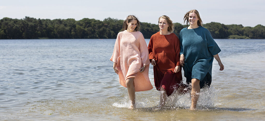 vrouwen met een zeemeermantel aan lopen door het water. De zeemeermantel is hun mooie en handige omkleedponcho.